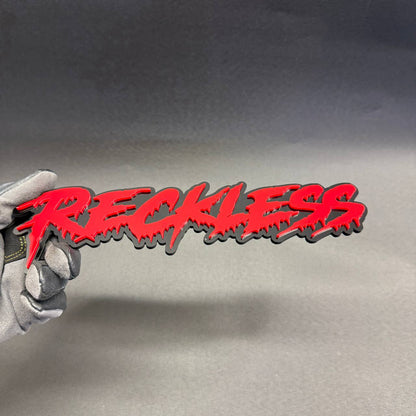Reckless red dripping graffiti script badge with glossy black background for Chevrolet Camaro Corvette performance car styling.