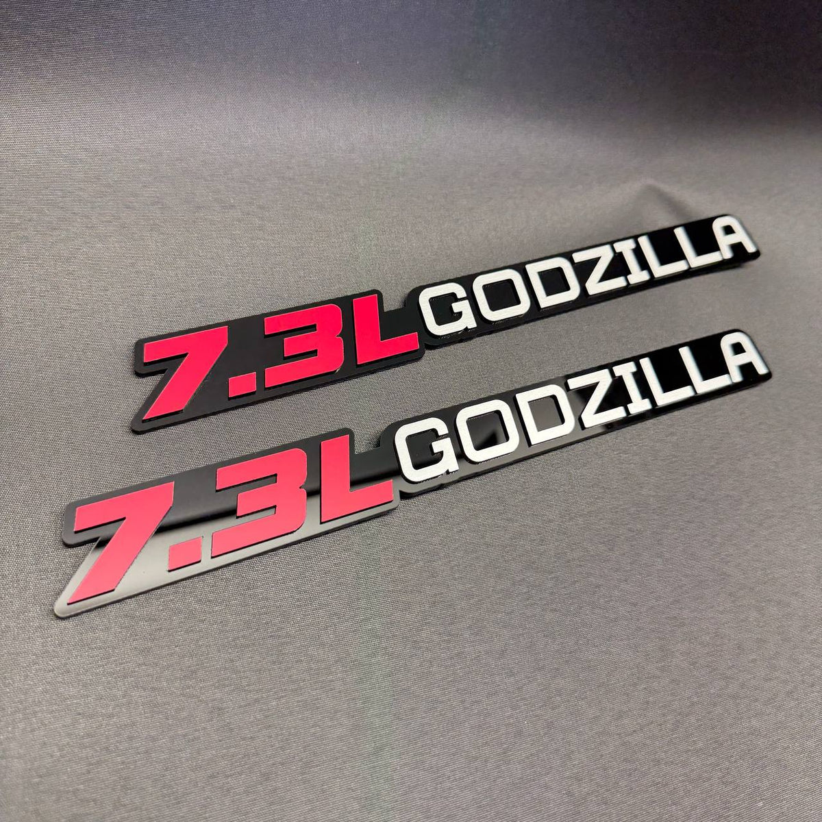 Aftermarket 7.3L Godzilla badge for Ford F-Series trucks, featuring two background finishes and bold sporty lettering.