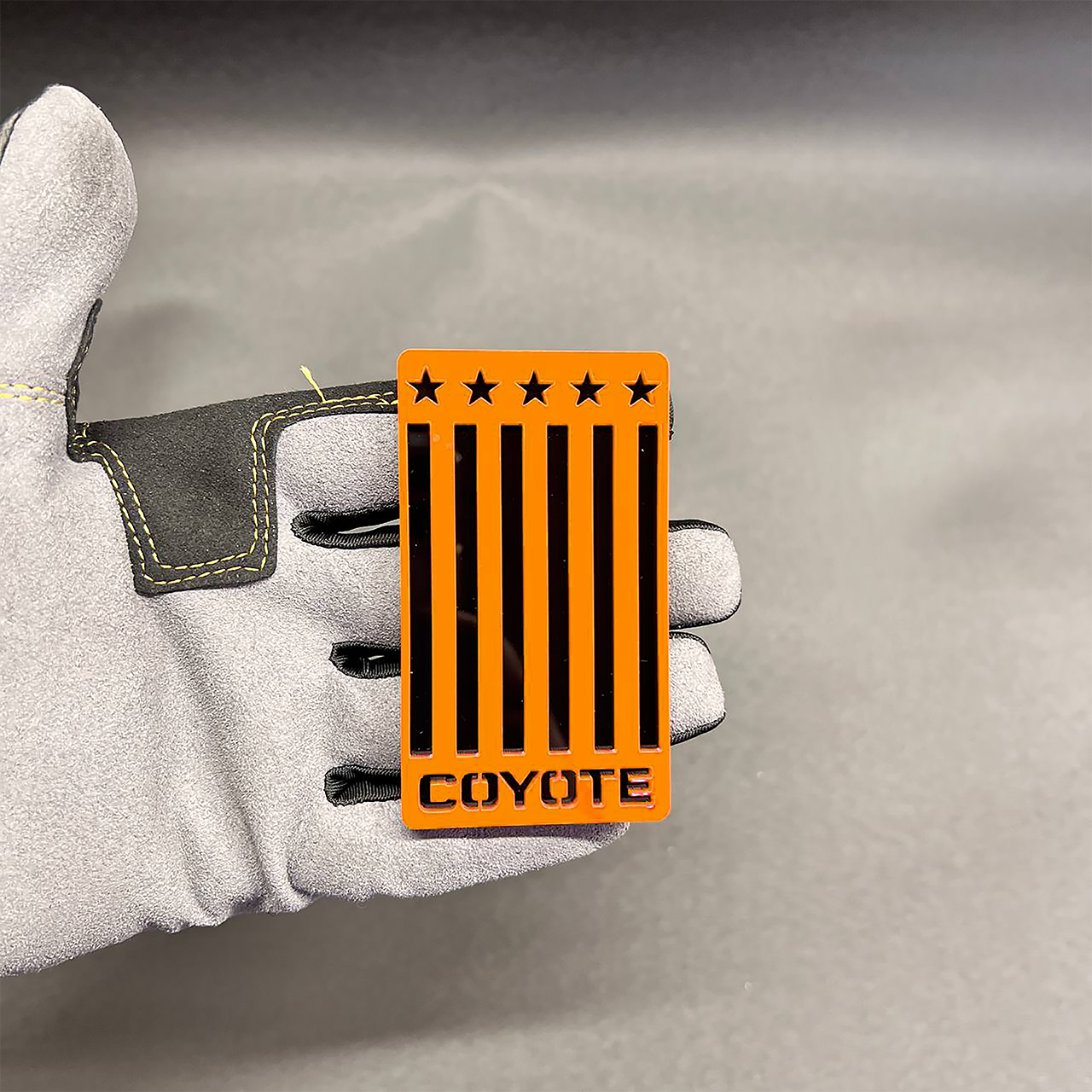 Acrylic Coyote flag emblem shown in hand with red base and black stripes for performance car styling.