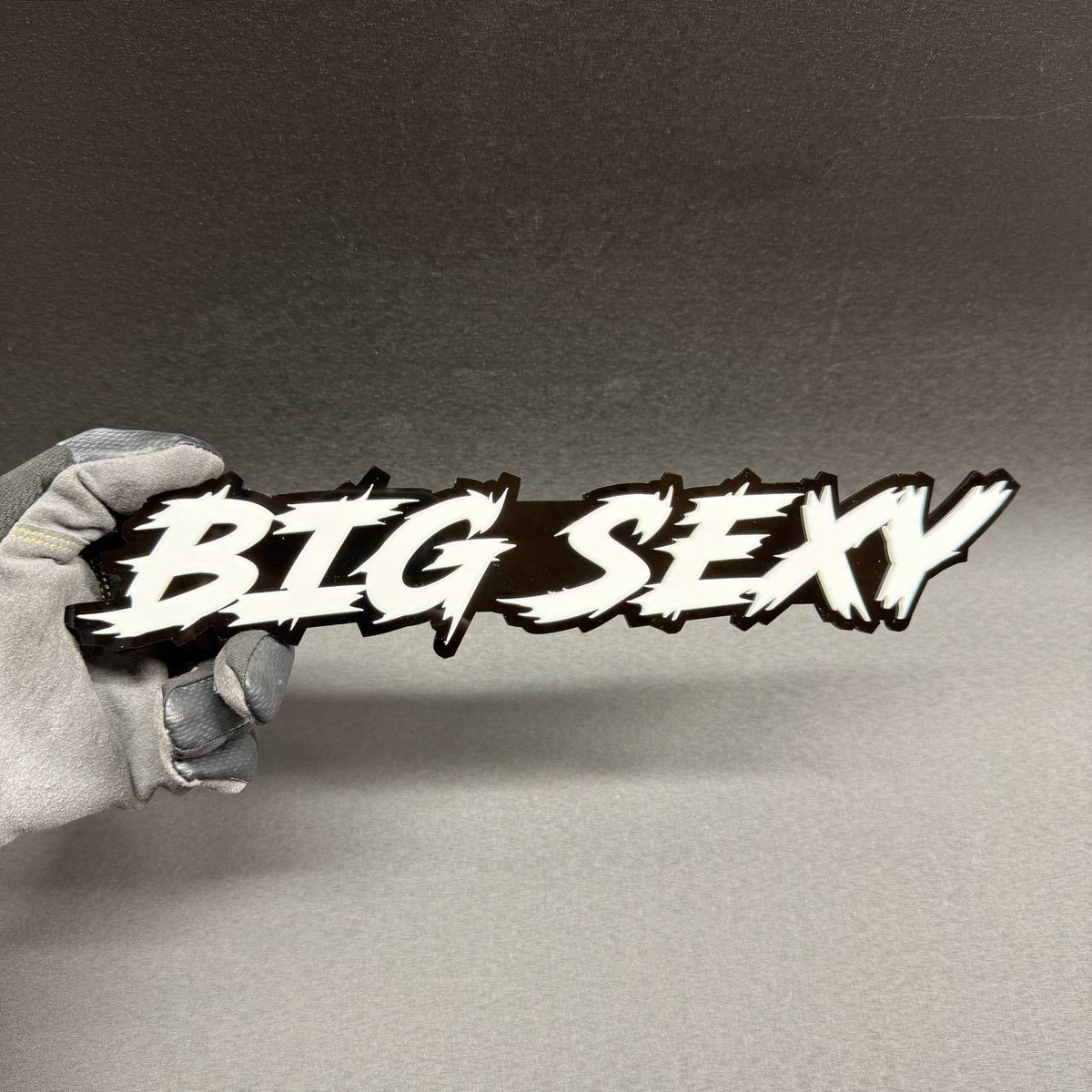 Big Sexy custom car text badge with white graffiti-style lettering and glossy black backing, aftermarket emblem for Ford F150, RAM 1500 and Chevy Silverado.