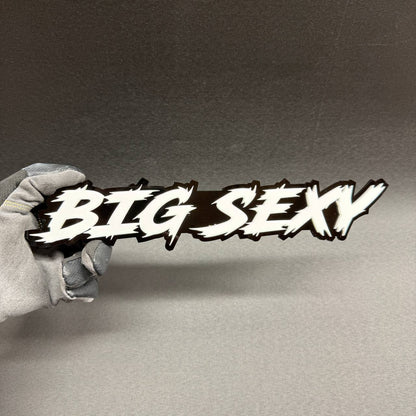 Big Sexy custom car text badge with white graffiti-style lettering and glossy black backing, aftermarket emblem for Ford F150, RAM 1500 and Chevy Silverado.