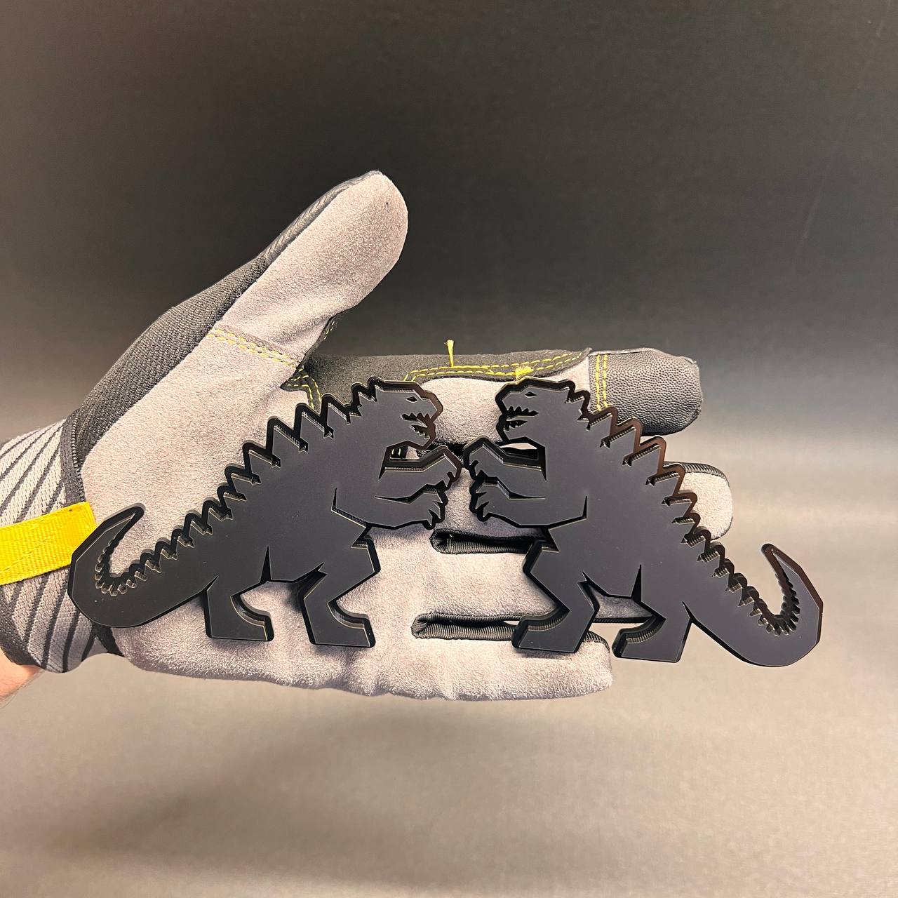 Glossy black Godzilla style automotive emblem featuring a bold dinosaur design with adhesive backing.