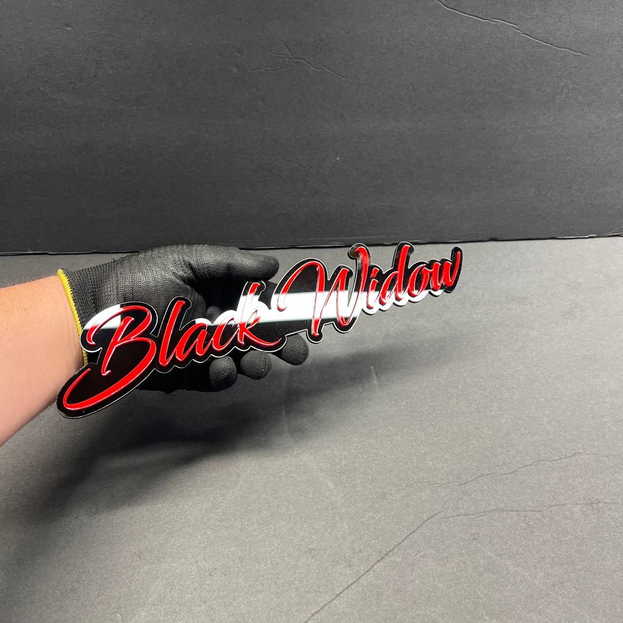 Black Widow red drip automotive emblem held in hand, glossy acrylic finish