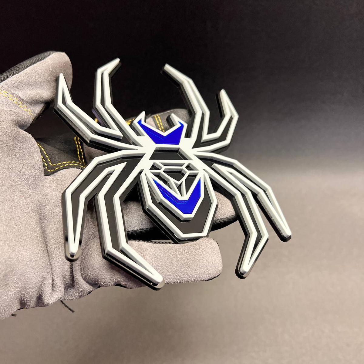 Gray black spider fender emblem with glossy mirror blue details for custom car exterior styling.