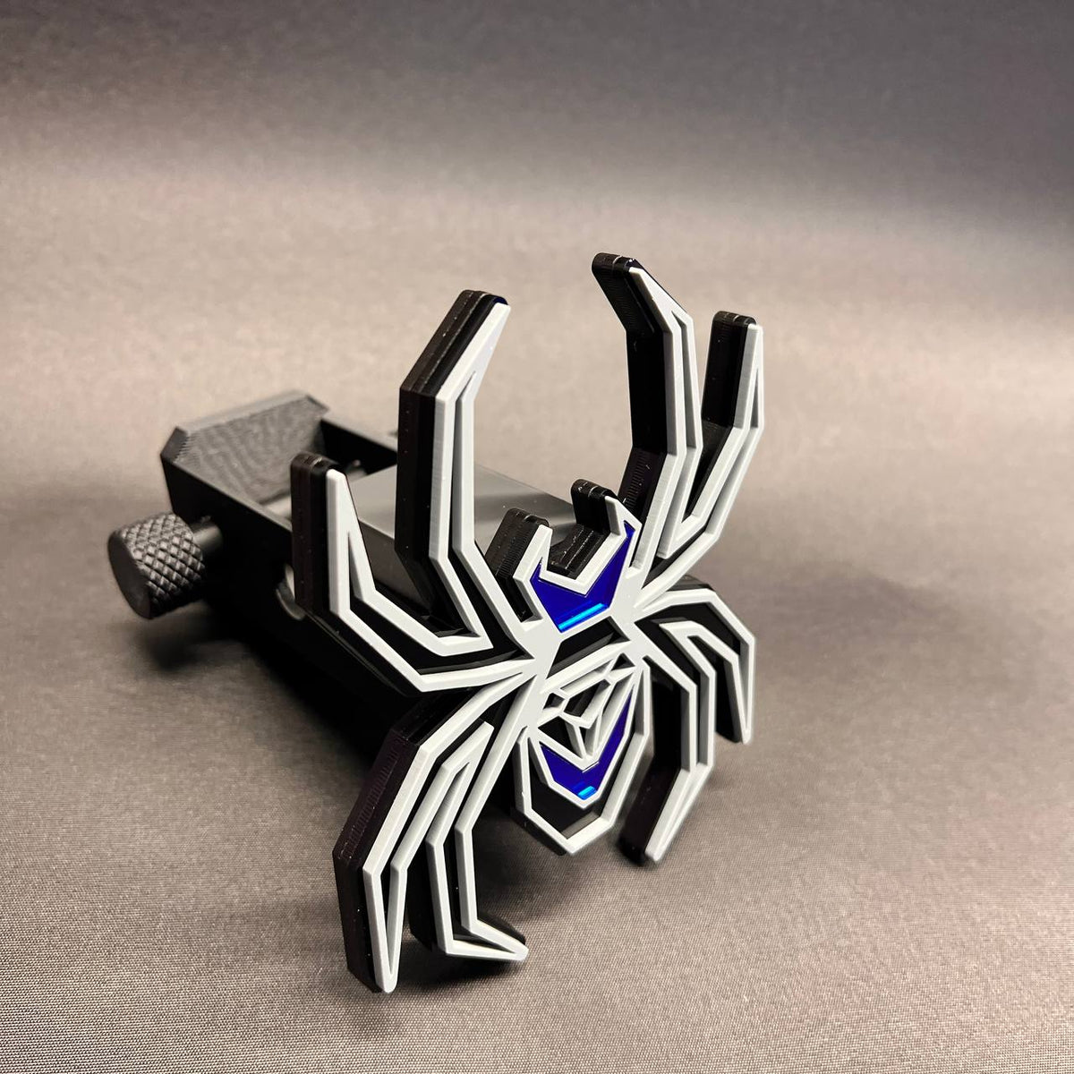 Gray on black Black Widow spider car badge with reflective mirror blue accent sections.