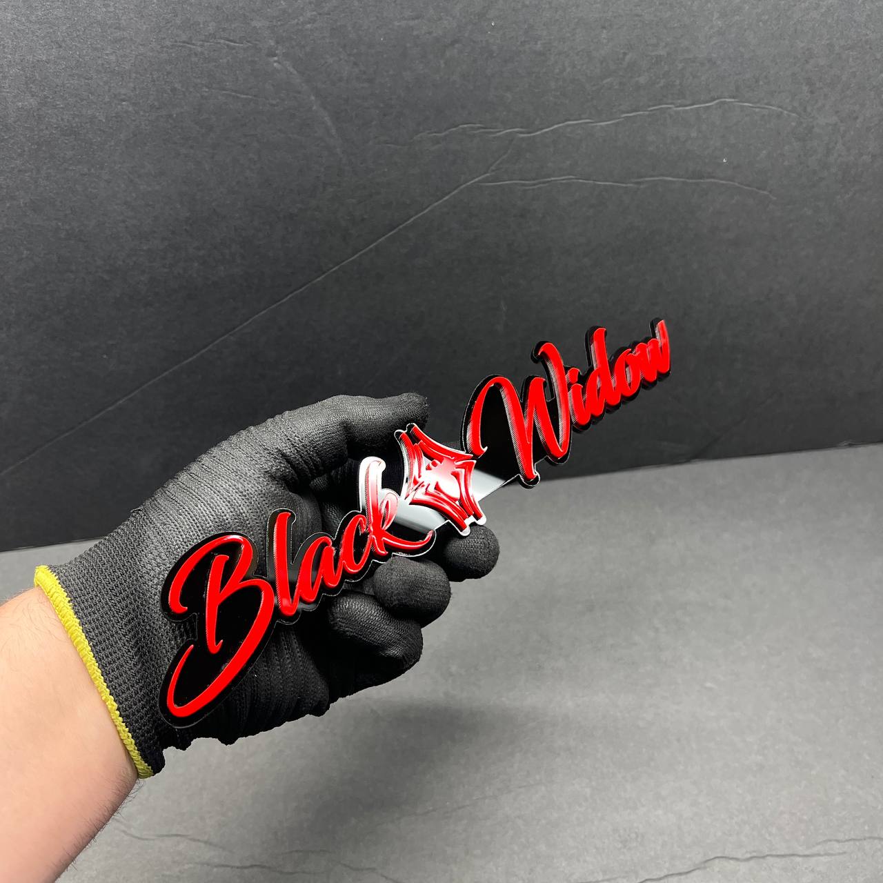 Black Widow red drip automotive emblem held in hand, glossy acrylic finish