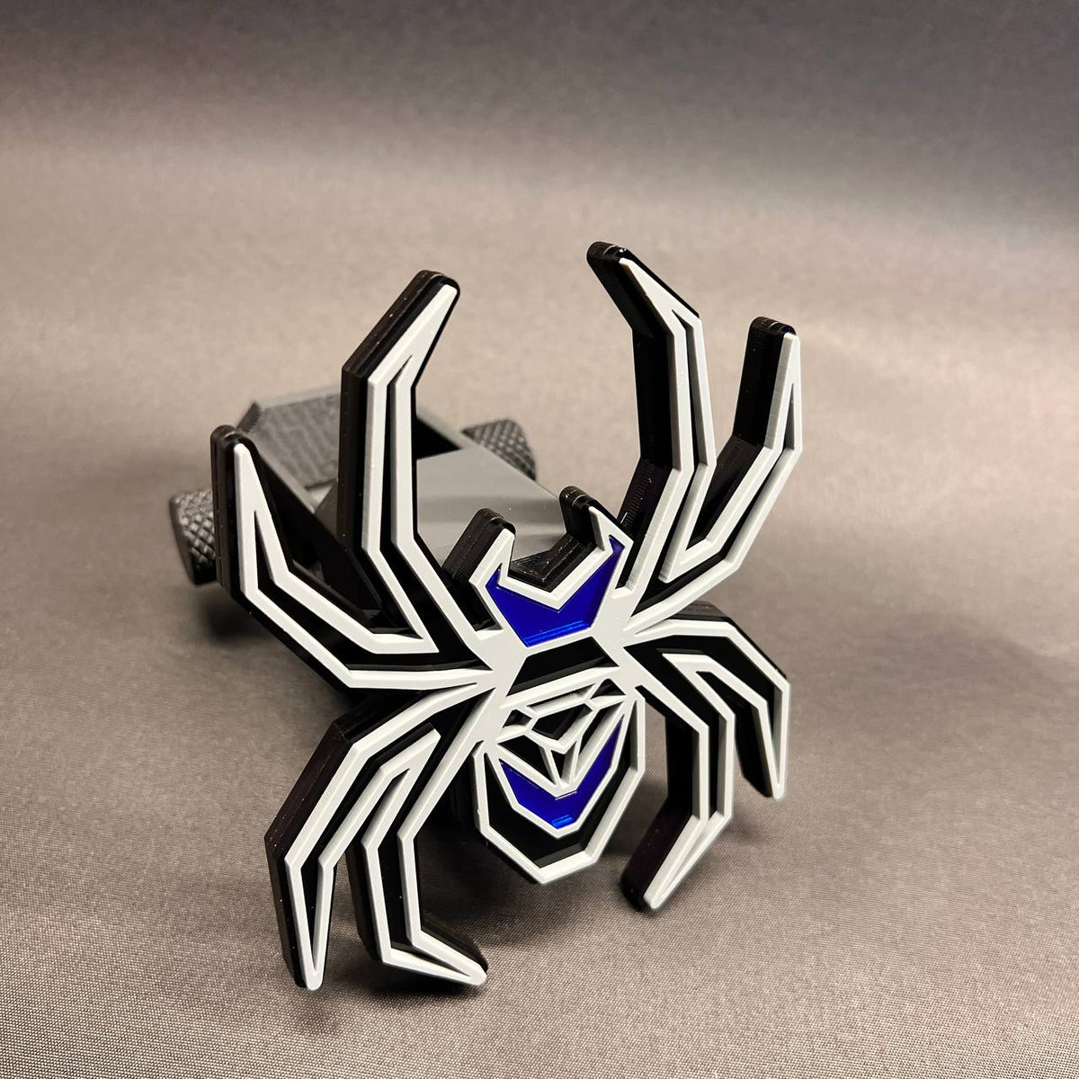 Black Widow spider receiver hitch cover with gray detailing and reflective blue accents.
