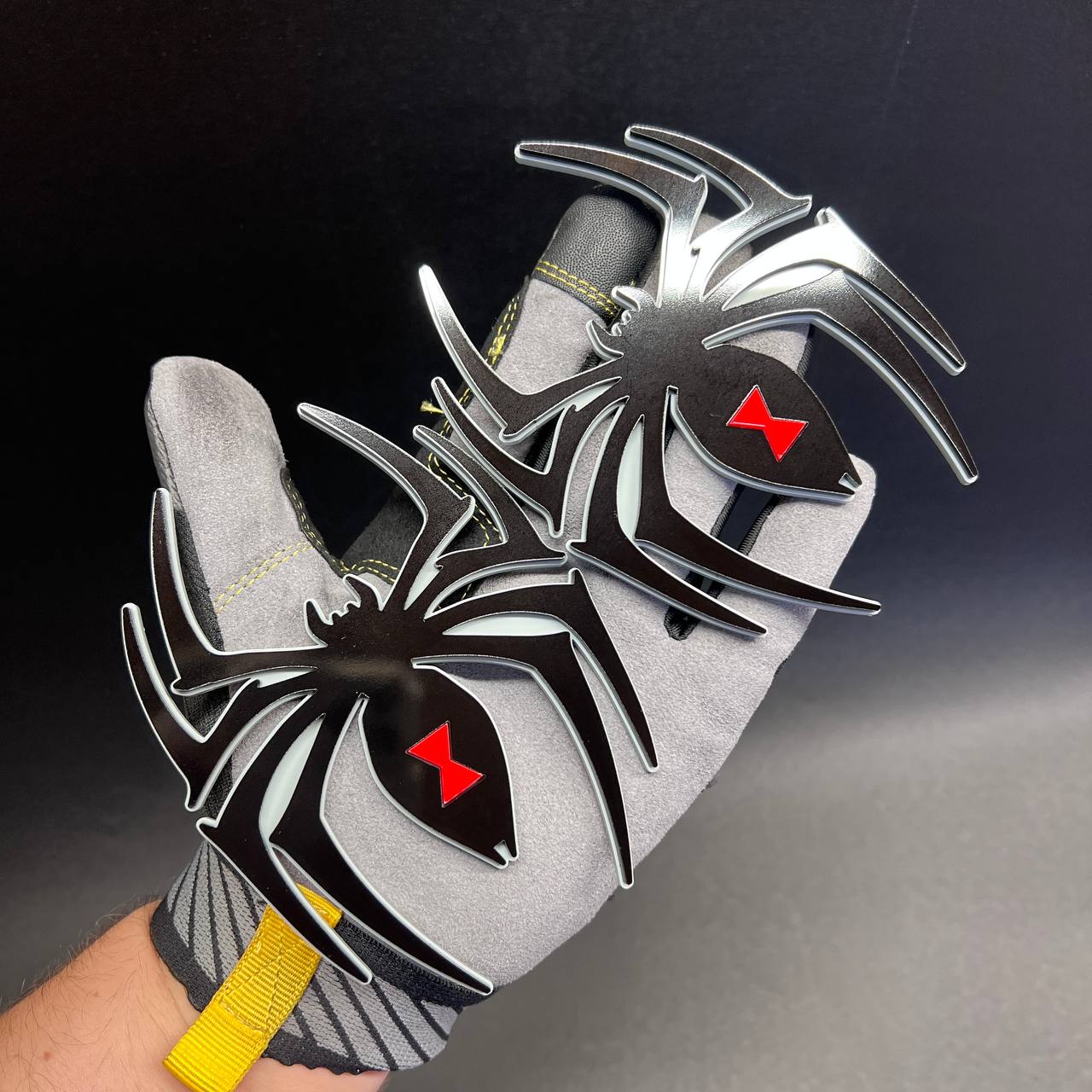Decorative Black Widow spider vehicle badge pair shown on a gloved hand for size reference