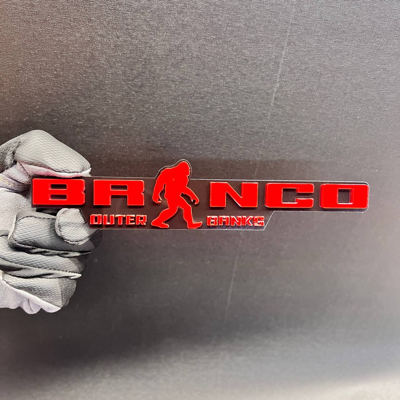 Red Bronco Outer Banks car emblem with Sasquatch silhouette and black background