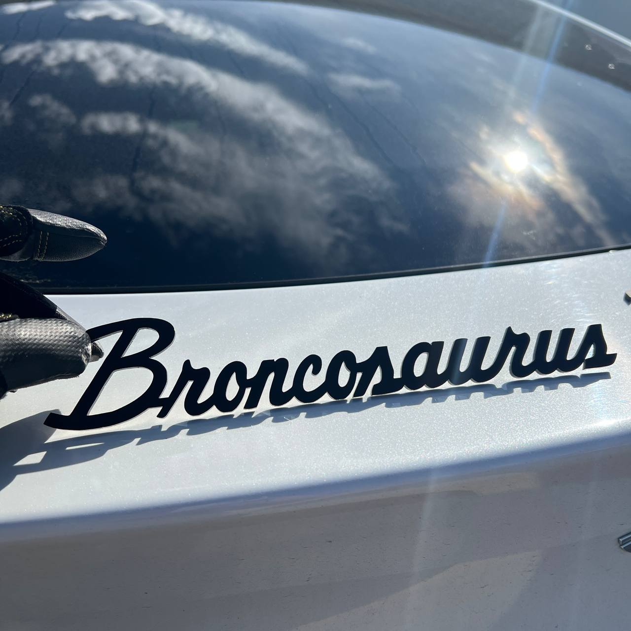 Broncosaurus script car emblem shown in hand with black finish