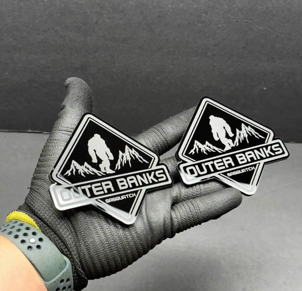 Outer Banks Sasquatch engraved automotive badge with black border and off-road style design