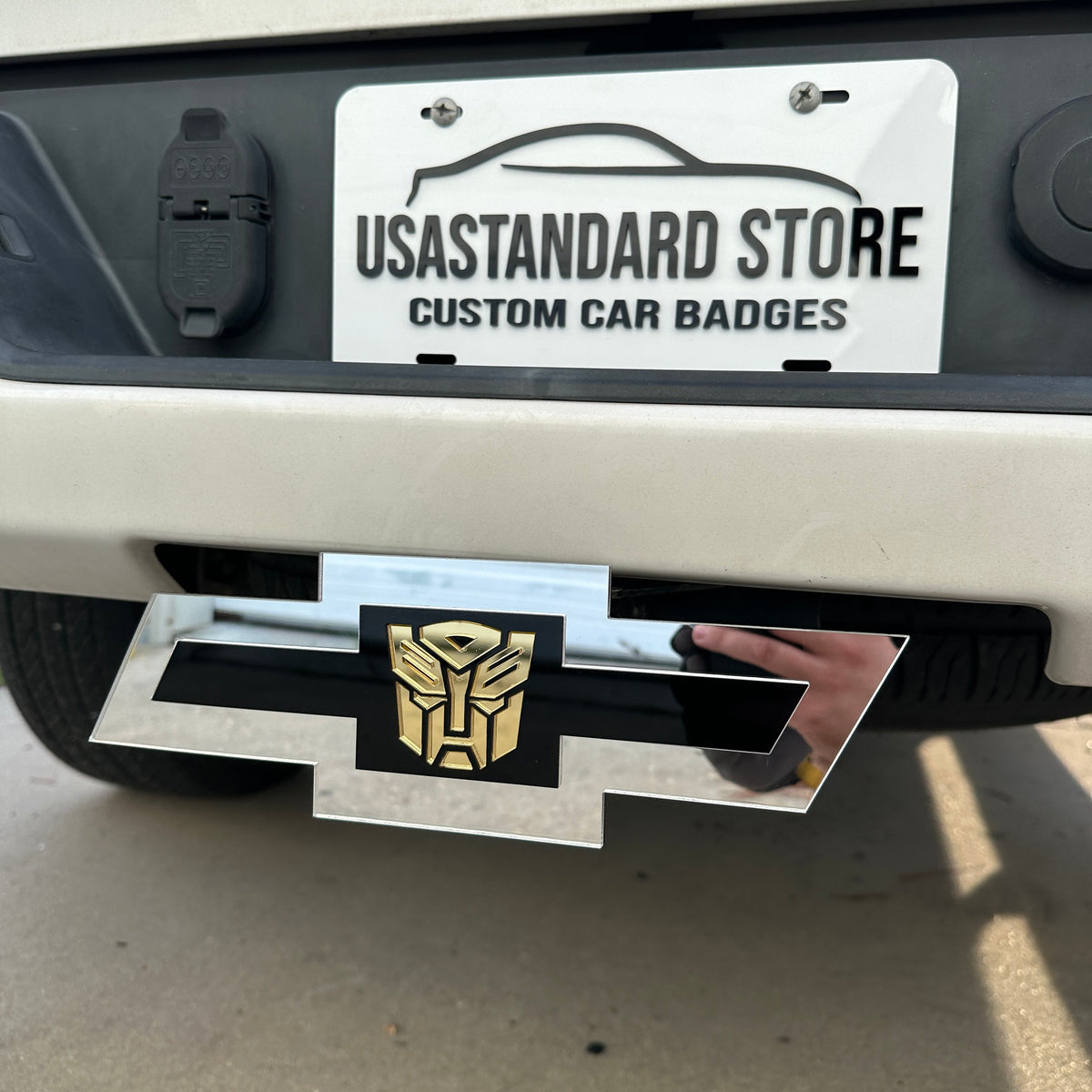Silver Chevy Bowtie hitch cover with gold Autobot emblem mounted on truck receiver
