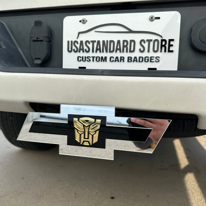 Silver Chevy Bowtie hitch cover with gold Autobot emblem mounted on truck receiver