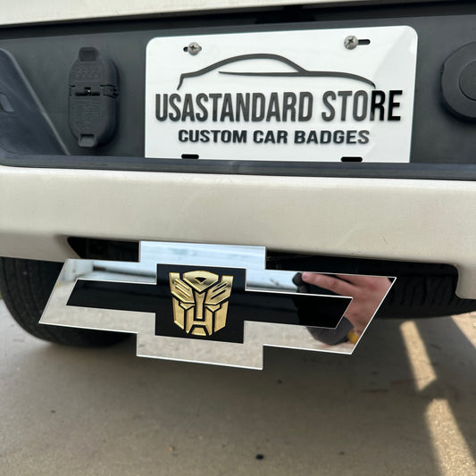 Silver Chevy Bowtie hitch cover with gold Autobot emblem mounted on truck receiver