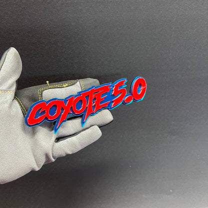 Glossy Coyote 5.0 car badge emblem shown on hand with red face and blue trim