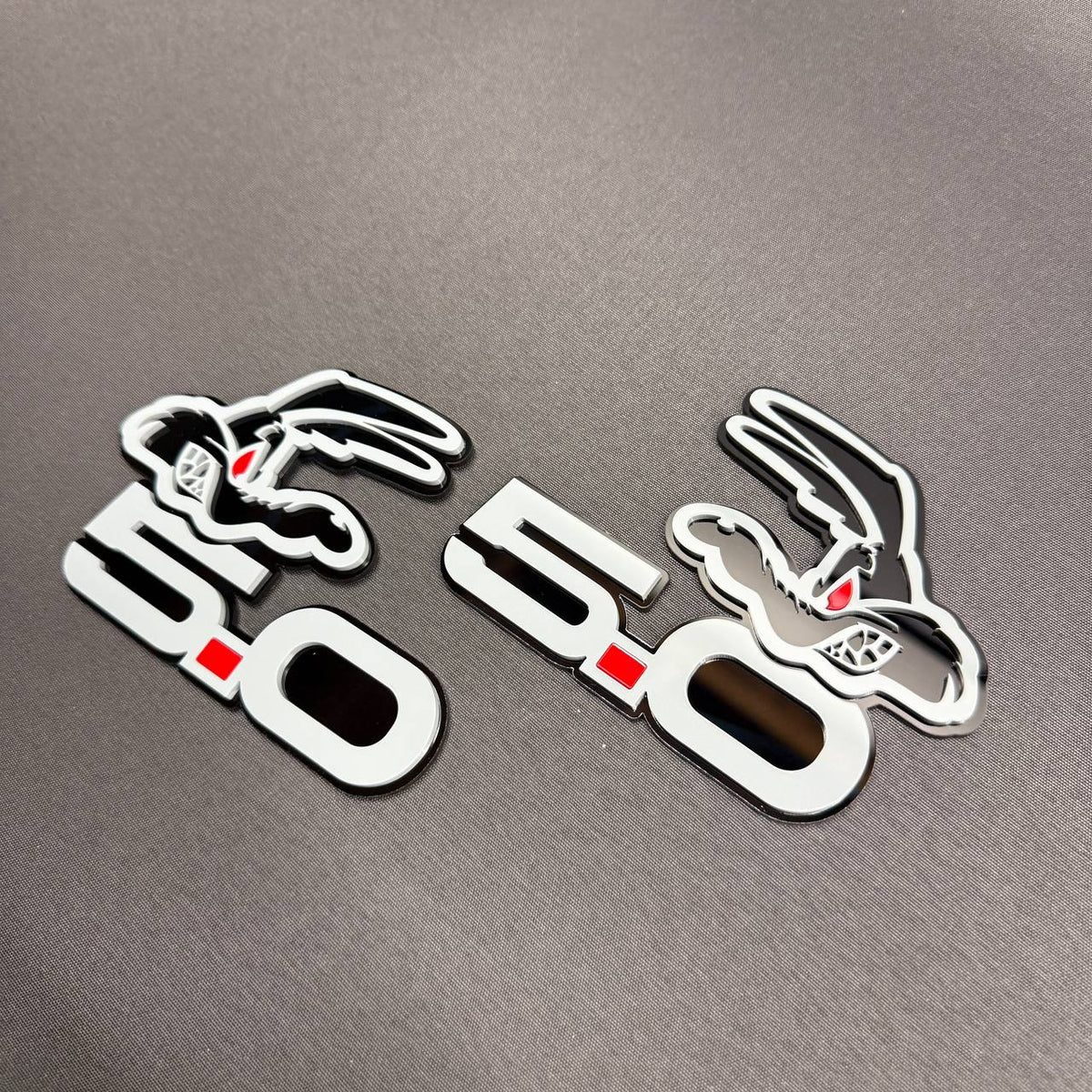 Ford F-150 Coyote 5.0 performance badge in gray and glossy black with red eye detailing and distinctive layered design.