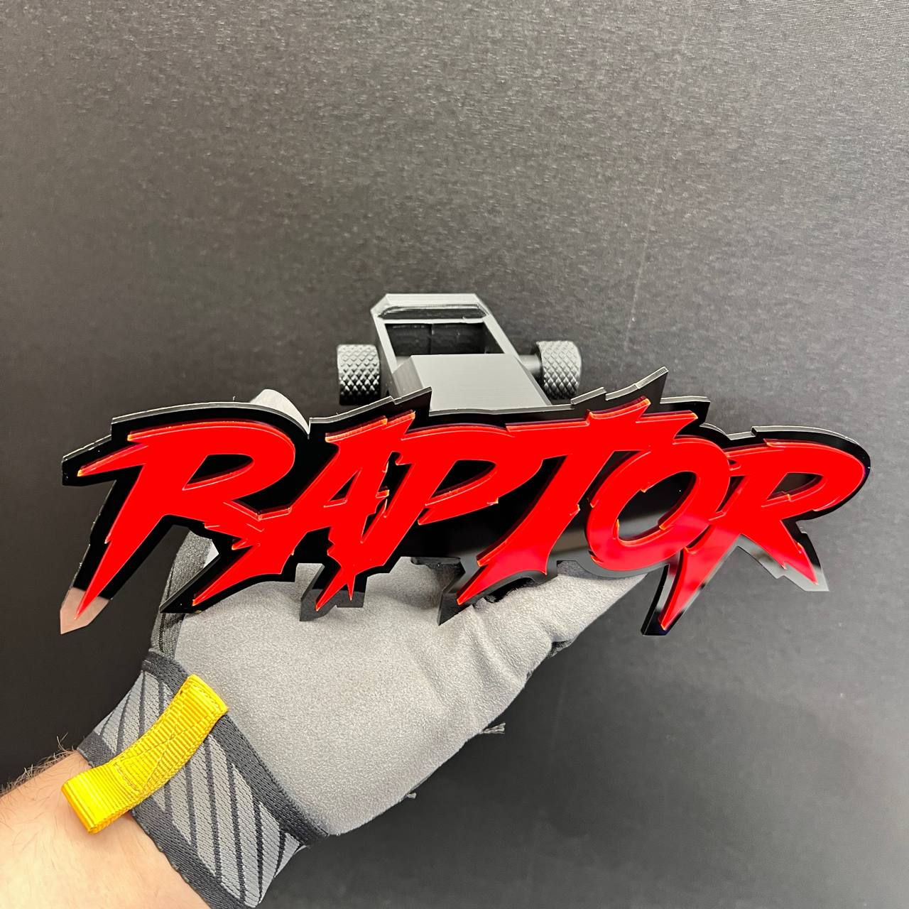 Red and black RAPTOR text badge mounted on a custom car hitch receiver cover