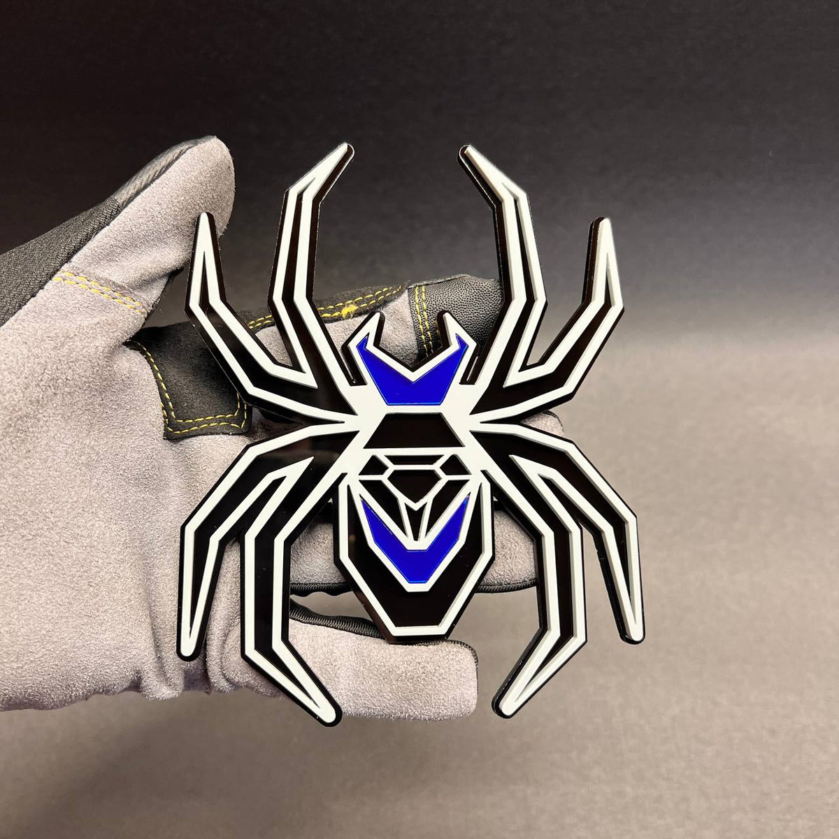 Black Widow fender badge with gray outline, black base, and bright mirror blue body accents.