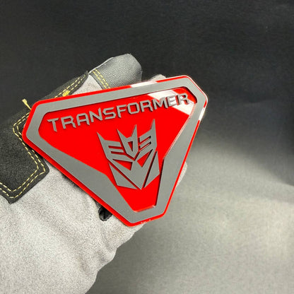 Decepticon Transformers automotive badge featuring angular shield borders, silver lettering and a detailed robot face emblem.