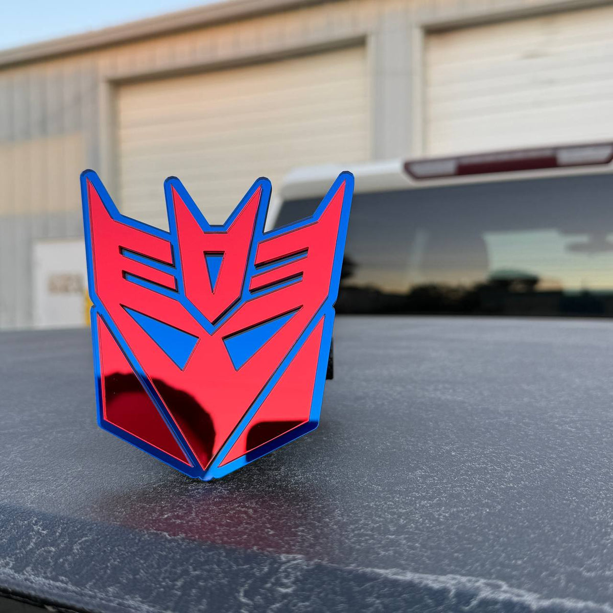 Red mirror and blue Transformers Decepticon emblem hitch cover for Dodge Ram 1500 pickup.