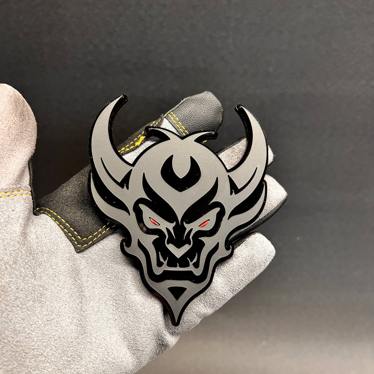 Demon Face adhesive car badge shown on glove with black and silver finish