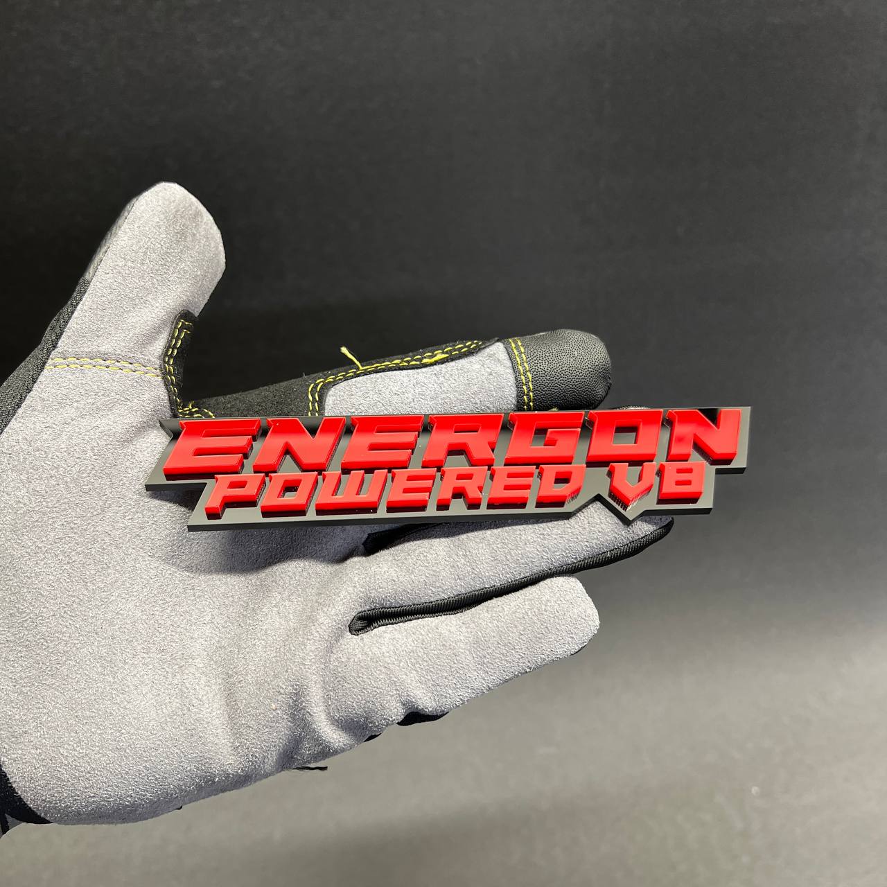 Custom ENERGON Powered V8 red and black acrylic text badge with raised lettering.