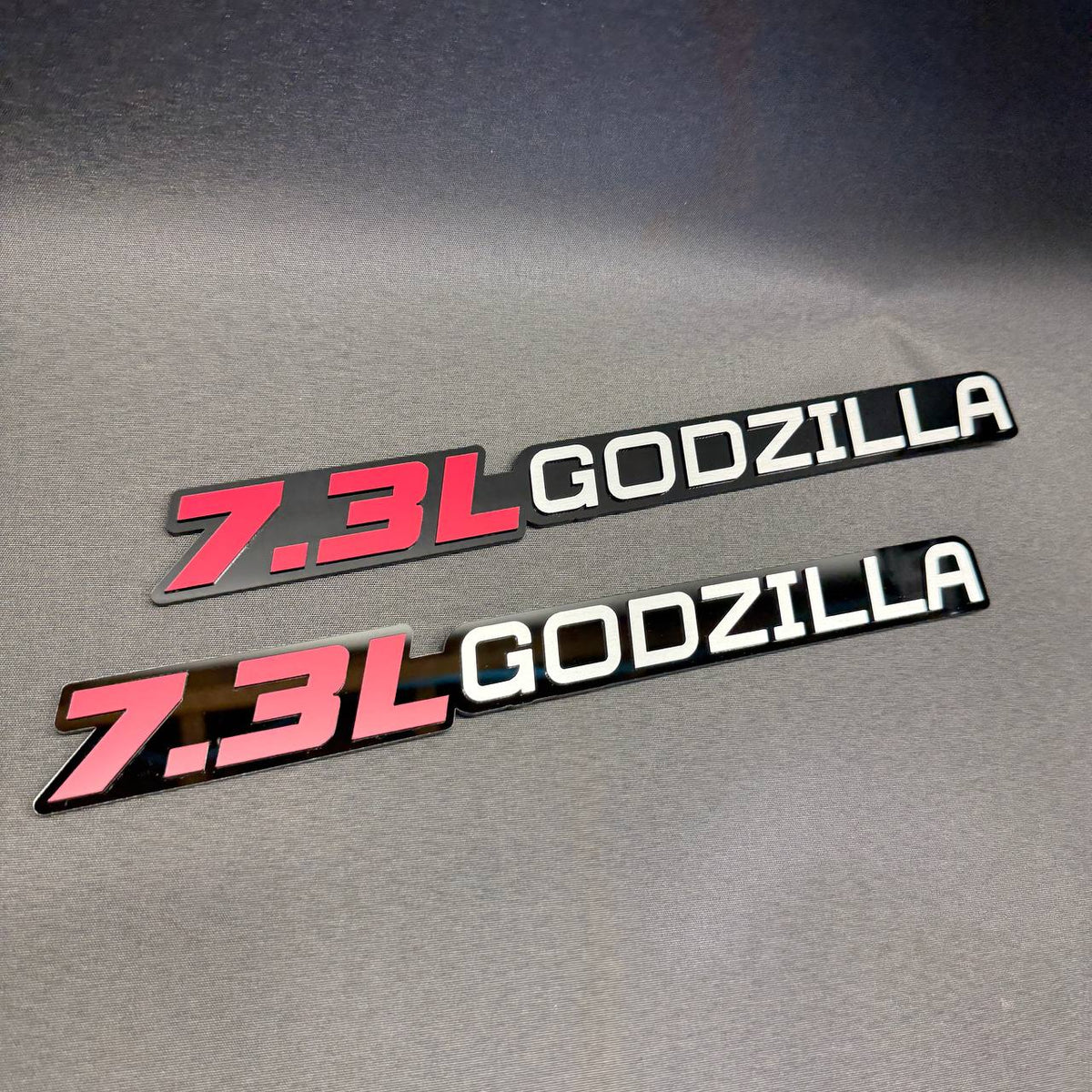 Ford 7.3L Godzilla V8 engine car badge with red lettering, white Godzilla text and glossy black background.