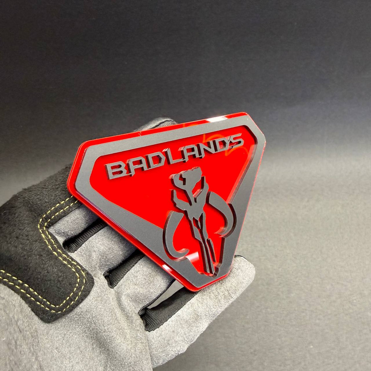 Mandalorian-inspired Mythosaur skull car emblem featuring Badlands lettering, black raised accents and a red shield-shaped background.