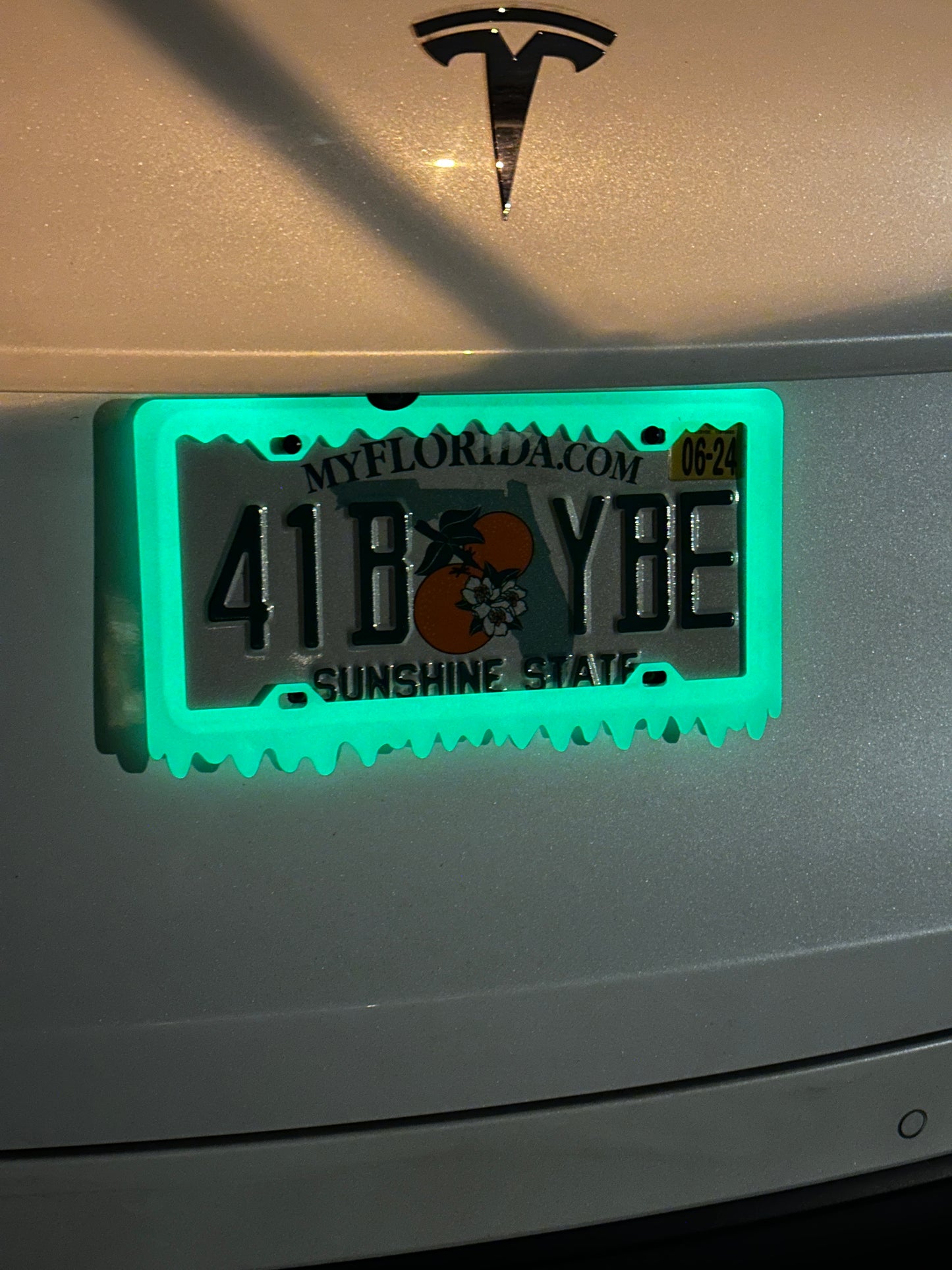 Car license plate frame glowing green around the plate at night