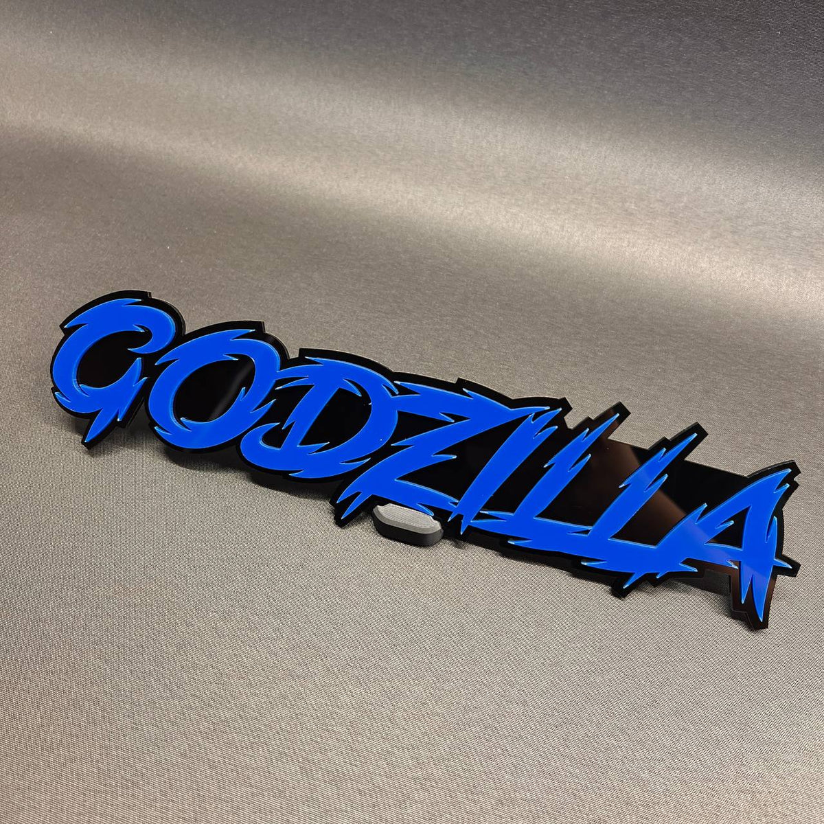 Godzilla auto badge with blue text and black backing for vehicle exterior