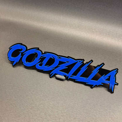 Godzilla auto badge with blue text and black backing for vehicle exterior