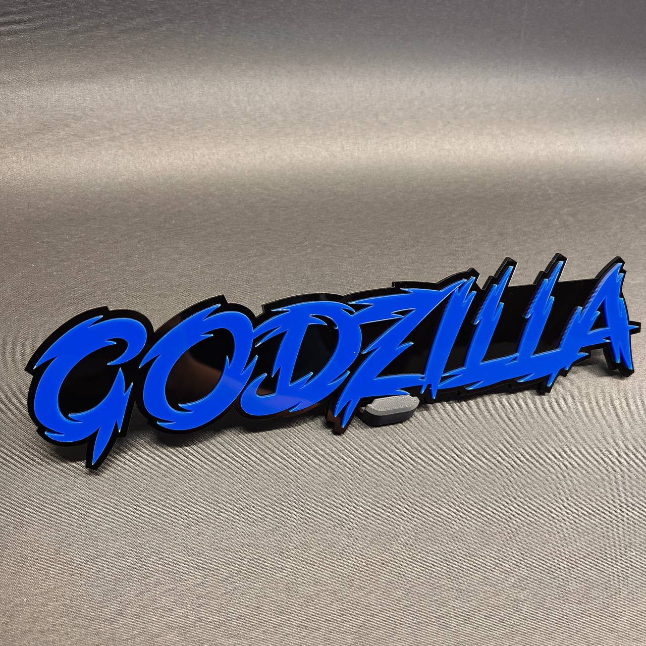 Godzilla auto badge with blue text and black backing for vehicle exterior