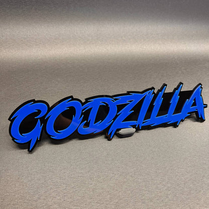 Godzilla auto badge with blue text and black backing for vehicle exterior
