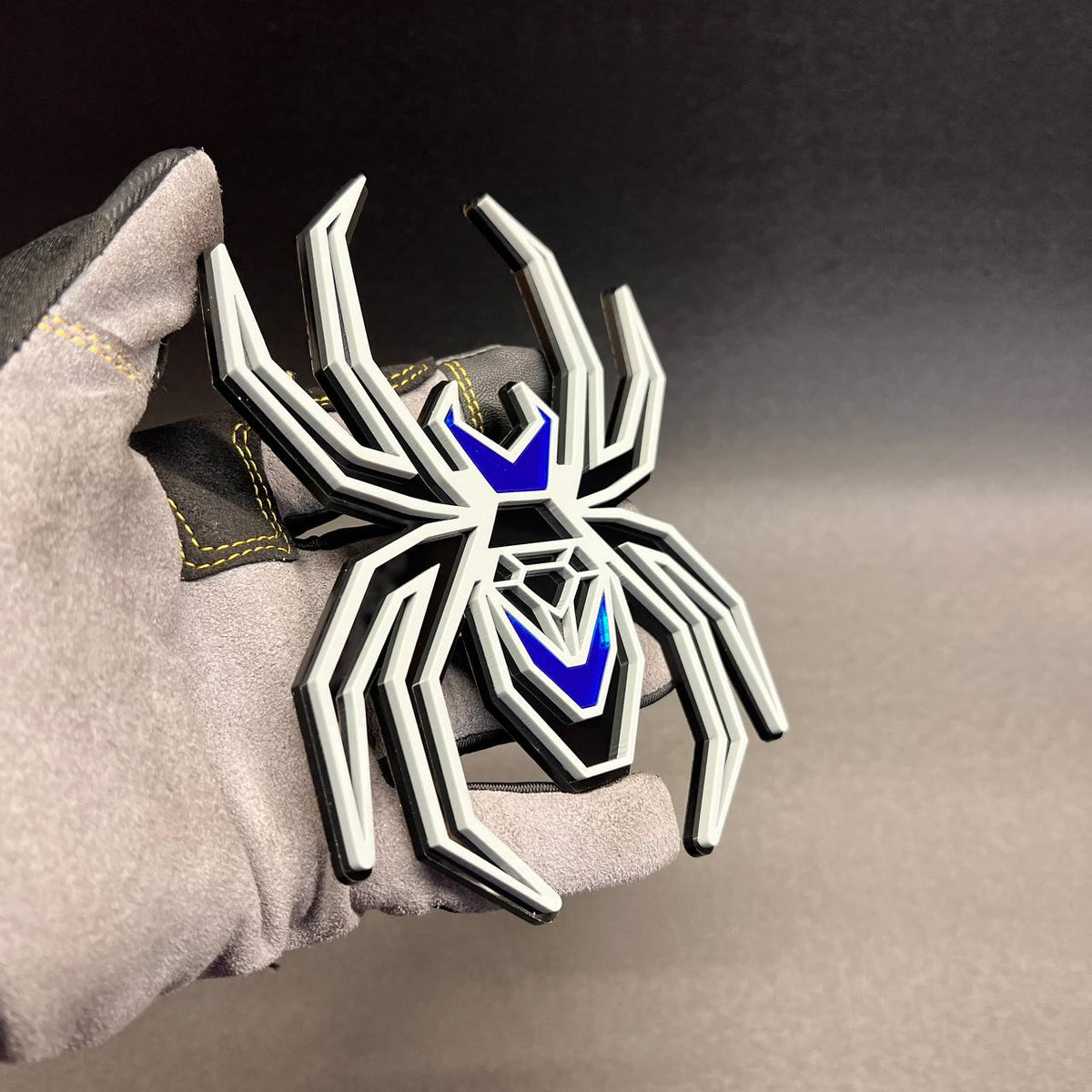 Gray and black spider car emblem featuring mirror blue accents and layered automotive design.