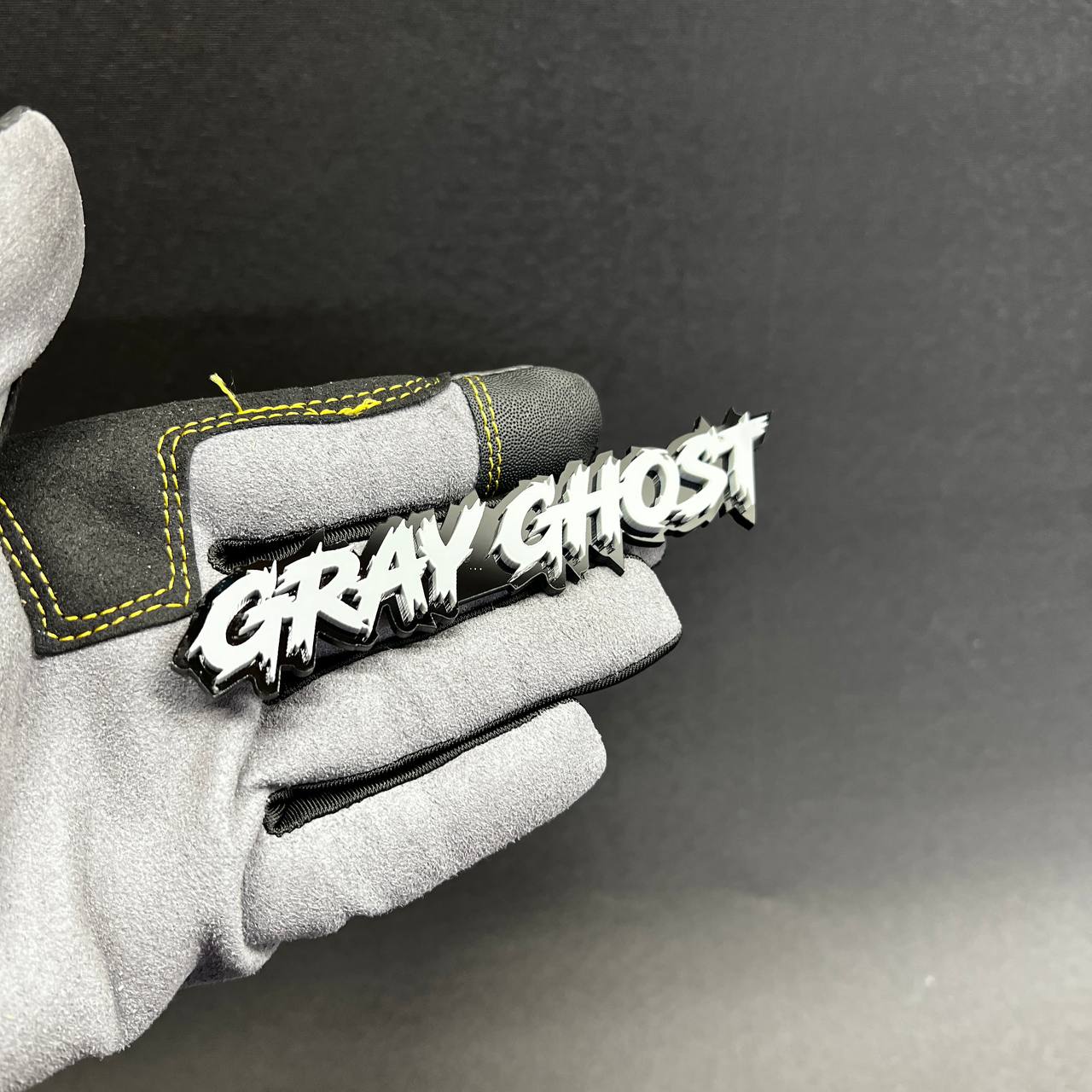 Gray Ghost Car Badge Fender Emblem shown on glove with white top and black backing