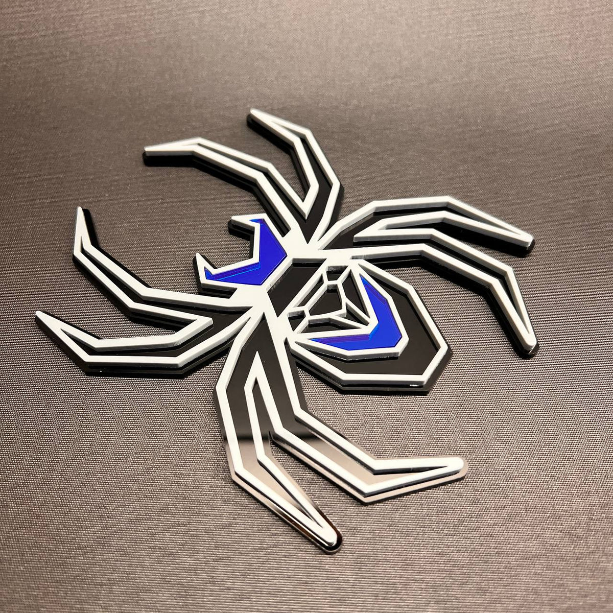 Custom spider car badge in gray on black with reflective blue details for fender installation.