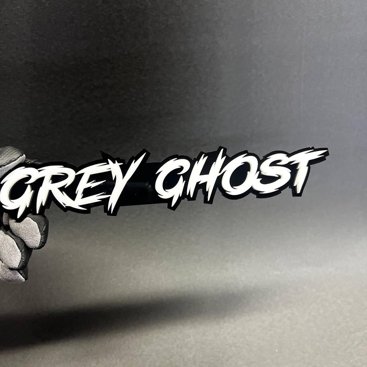 Grey Ghost script text car emblem shown in black and white layered acrylic for custom automotive decoration.