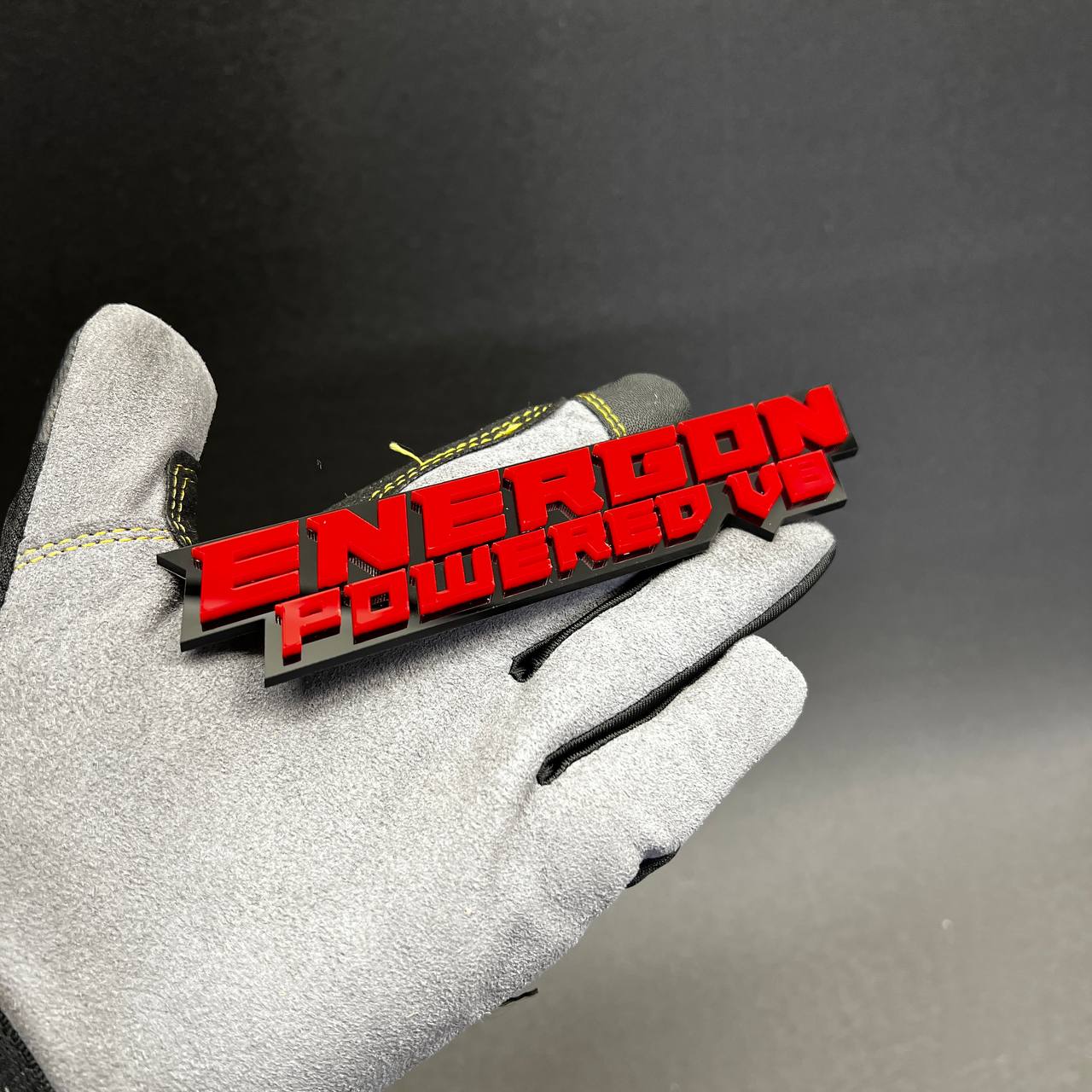 Gloss red ENERGON Powered V8 car badge fender emblem on black acrylic base.