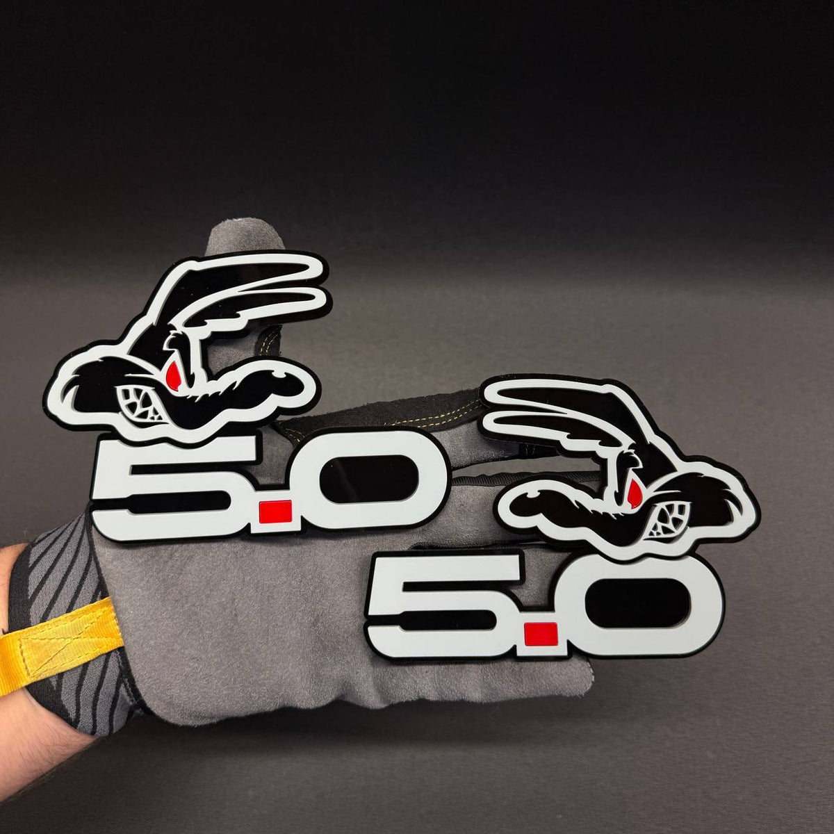 Mustang GT 5.0 Coyote fender badge in gray with red dot, glossy black background and detailed performance-inspired design.