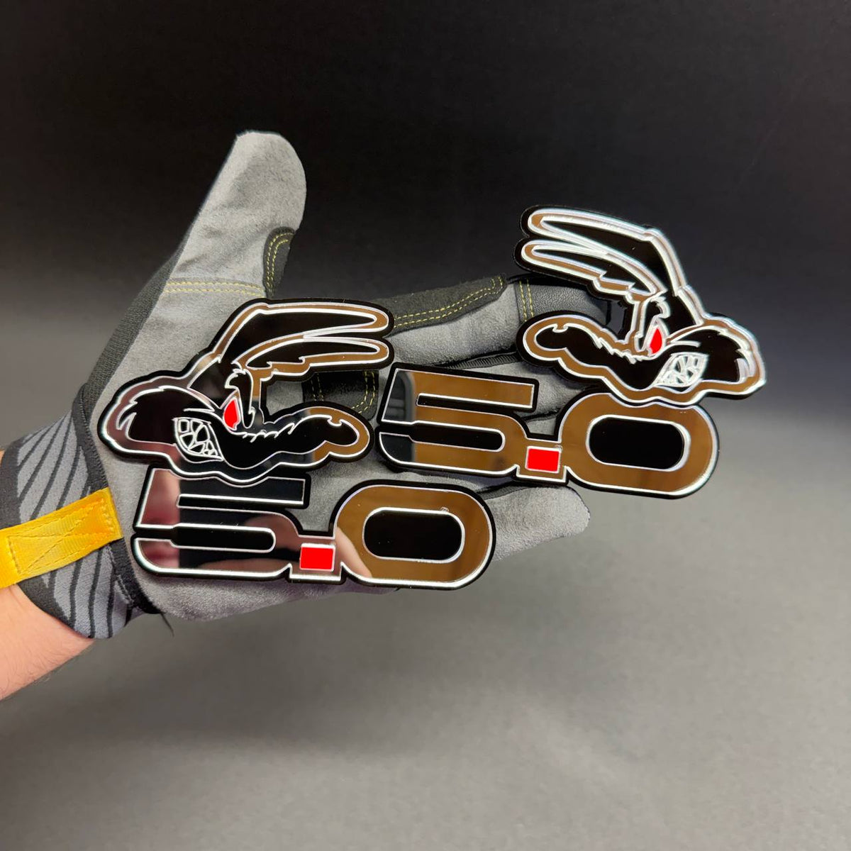 Custom Ford Coyote 5.0 V8 emblem displayed in hand showing reflective mirror silver finish and detailed layered construction.