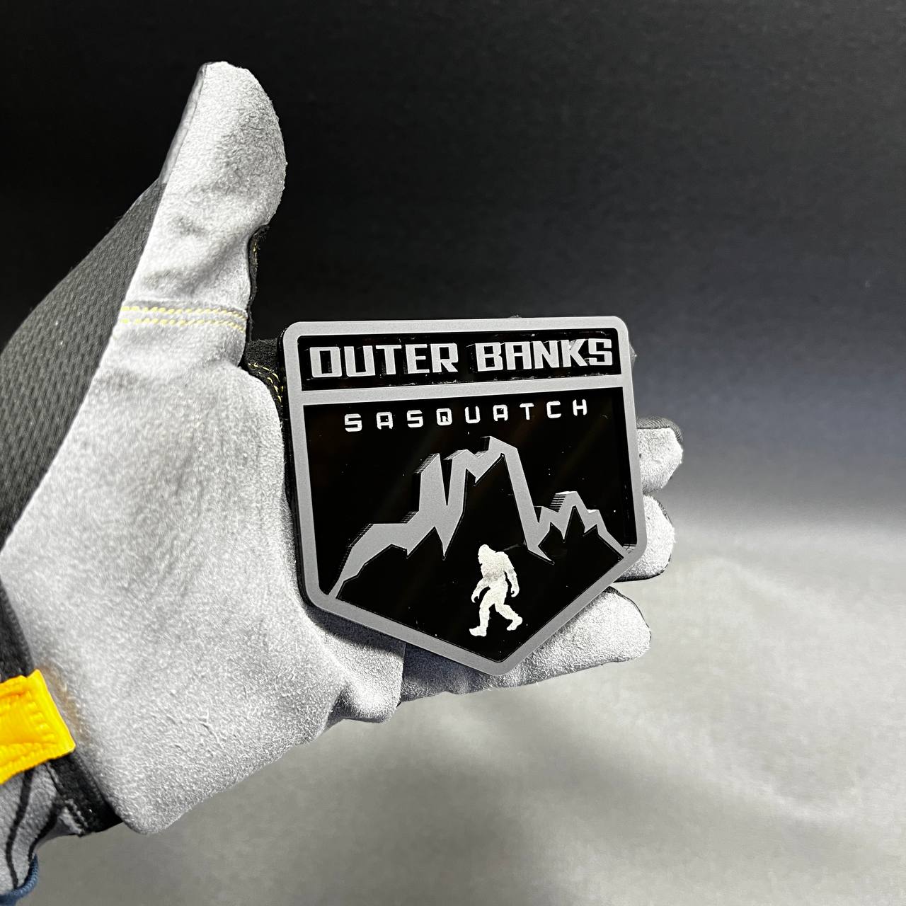 Outer Banks Sasquatch car badge with mountain and Bigfoot design