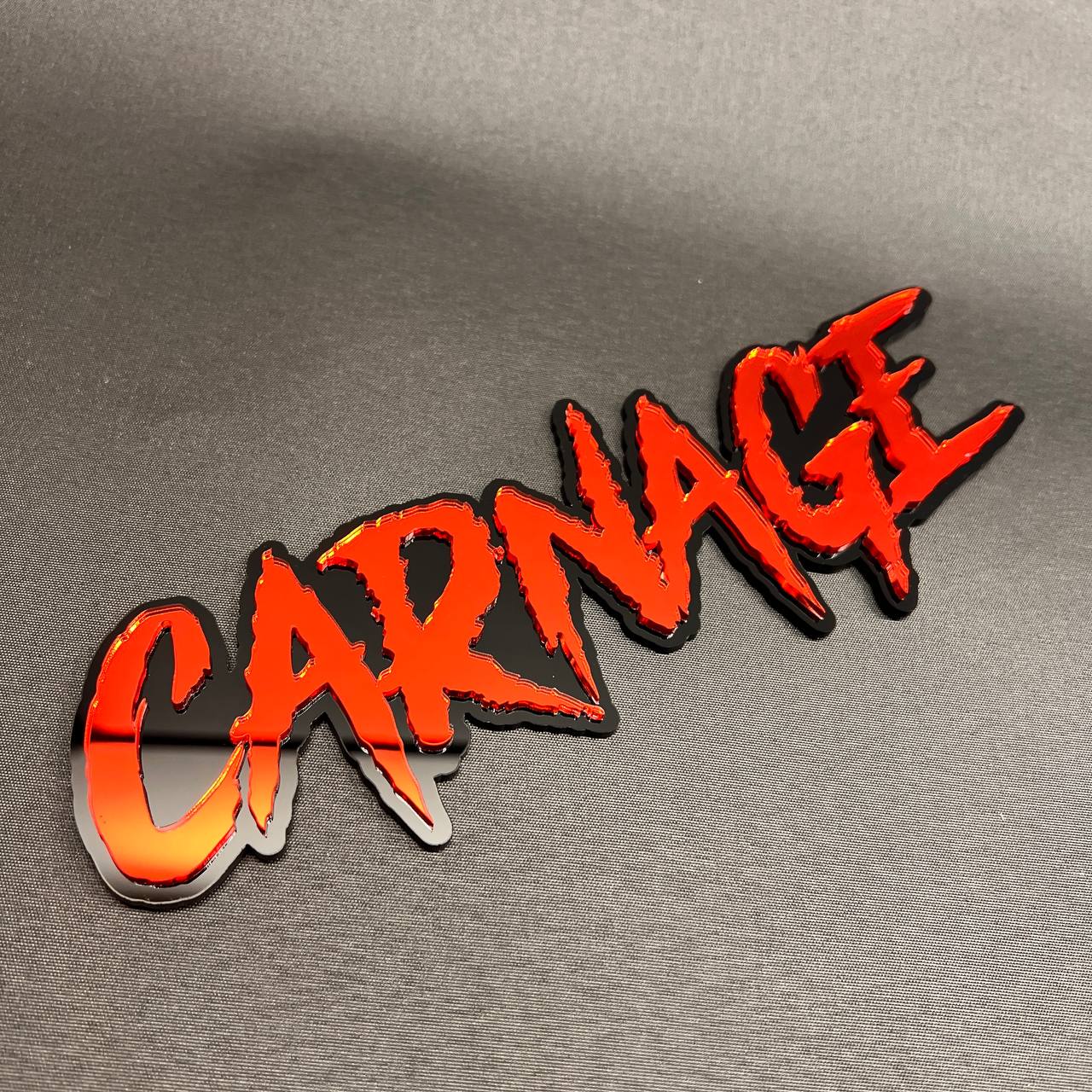 Red CARNAGE text car badge with black backing for custom automotive styling