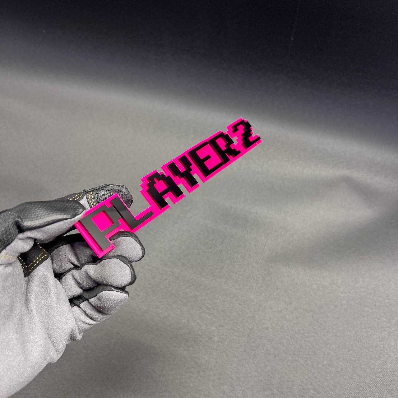 PLAYER 2 pixel style automotive badge with bold black lettering on pink base.