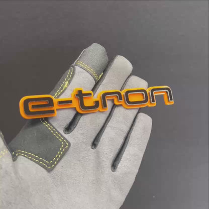 Orange and black E-TRON car badge shown on hand with glossy finish