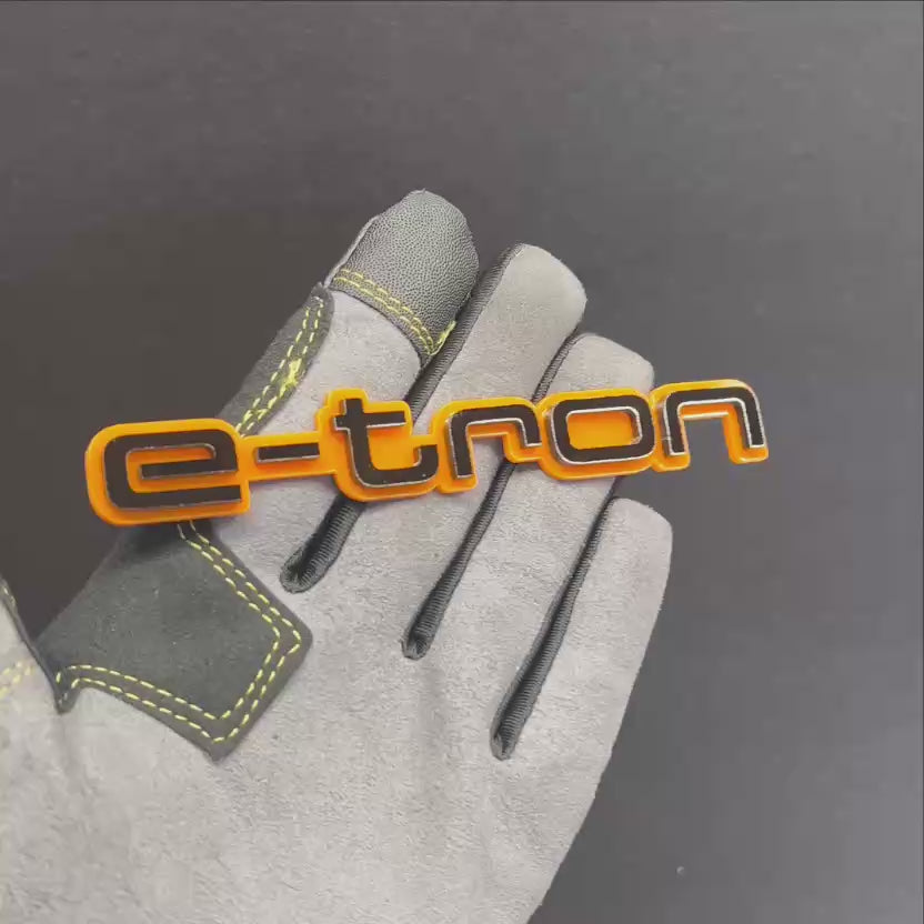 Orange and black E-TRON car badge shown on hand with glossy finish