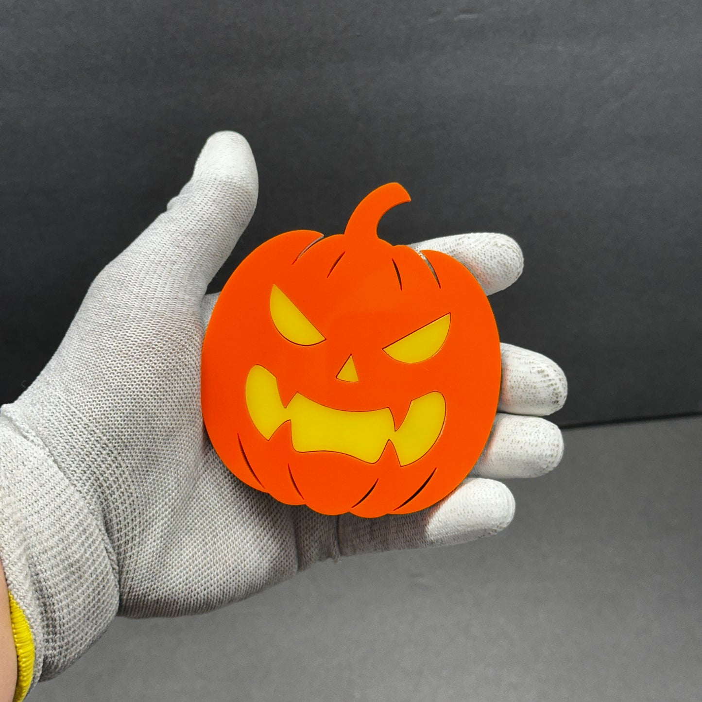 Orange jack-o-lantern car emblem shown in hand with yellow face detail