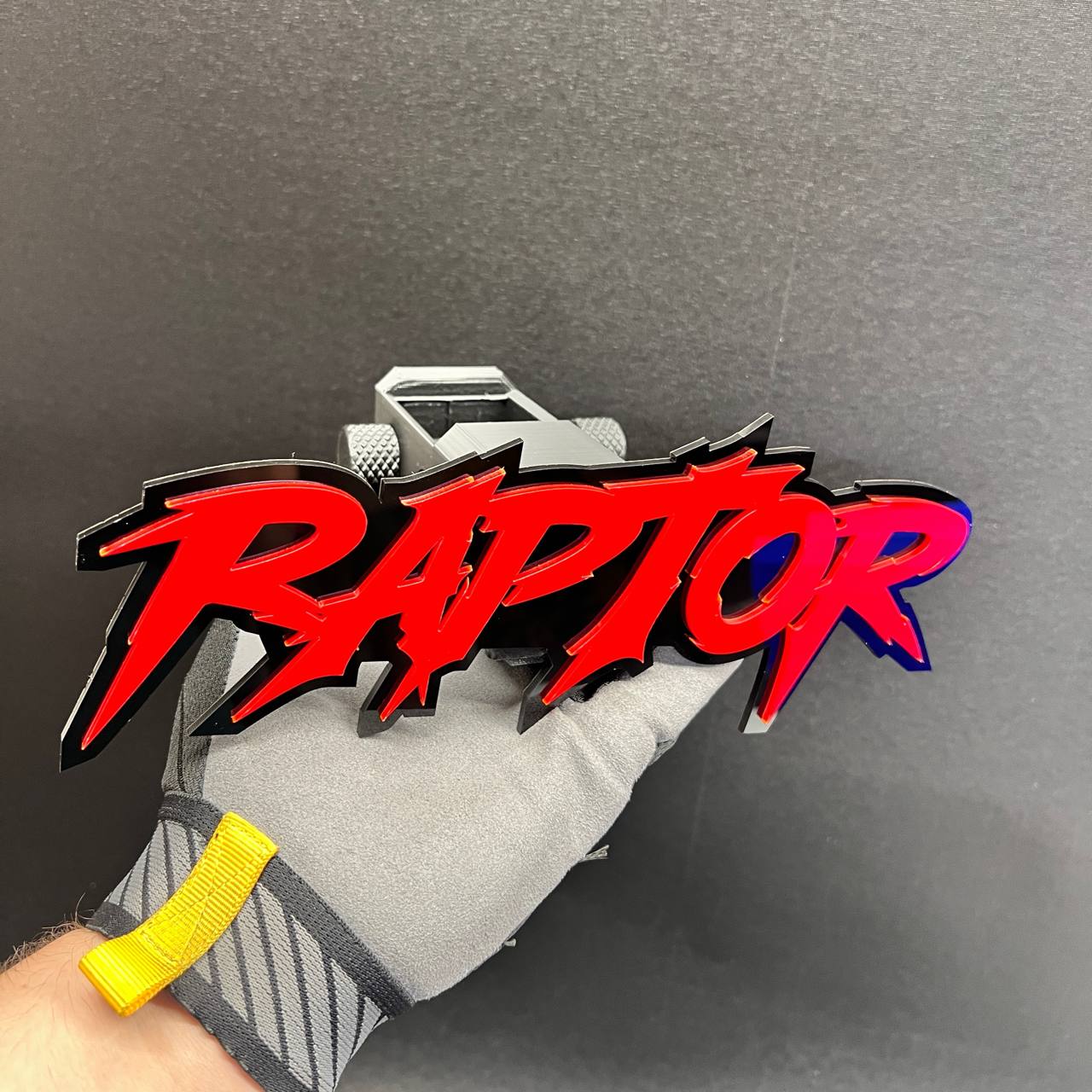 Red RAPTOR car badge hitch cover shown in a gloved hand