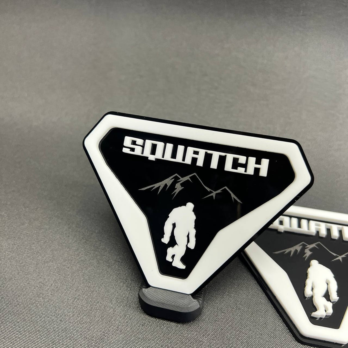 Sasquatch Bigfoot car badge in white on black with mountain artwork