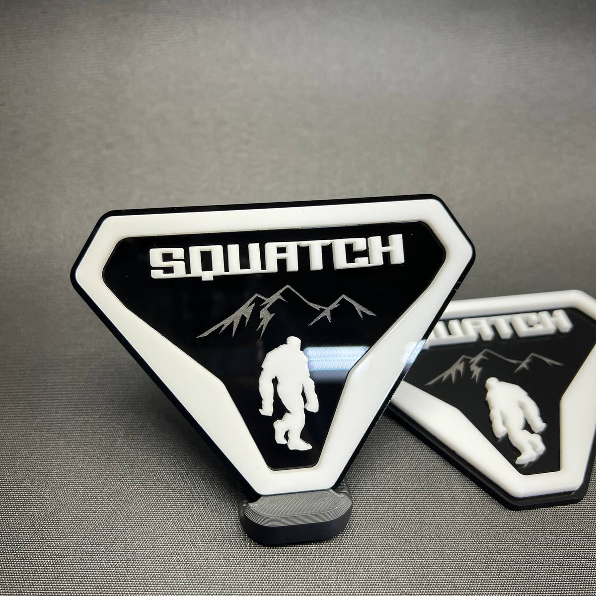 White and black Sasquatch car badge with raised lettering