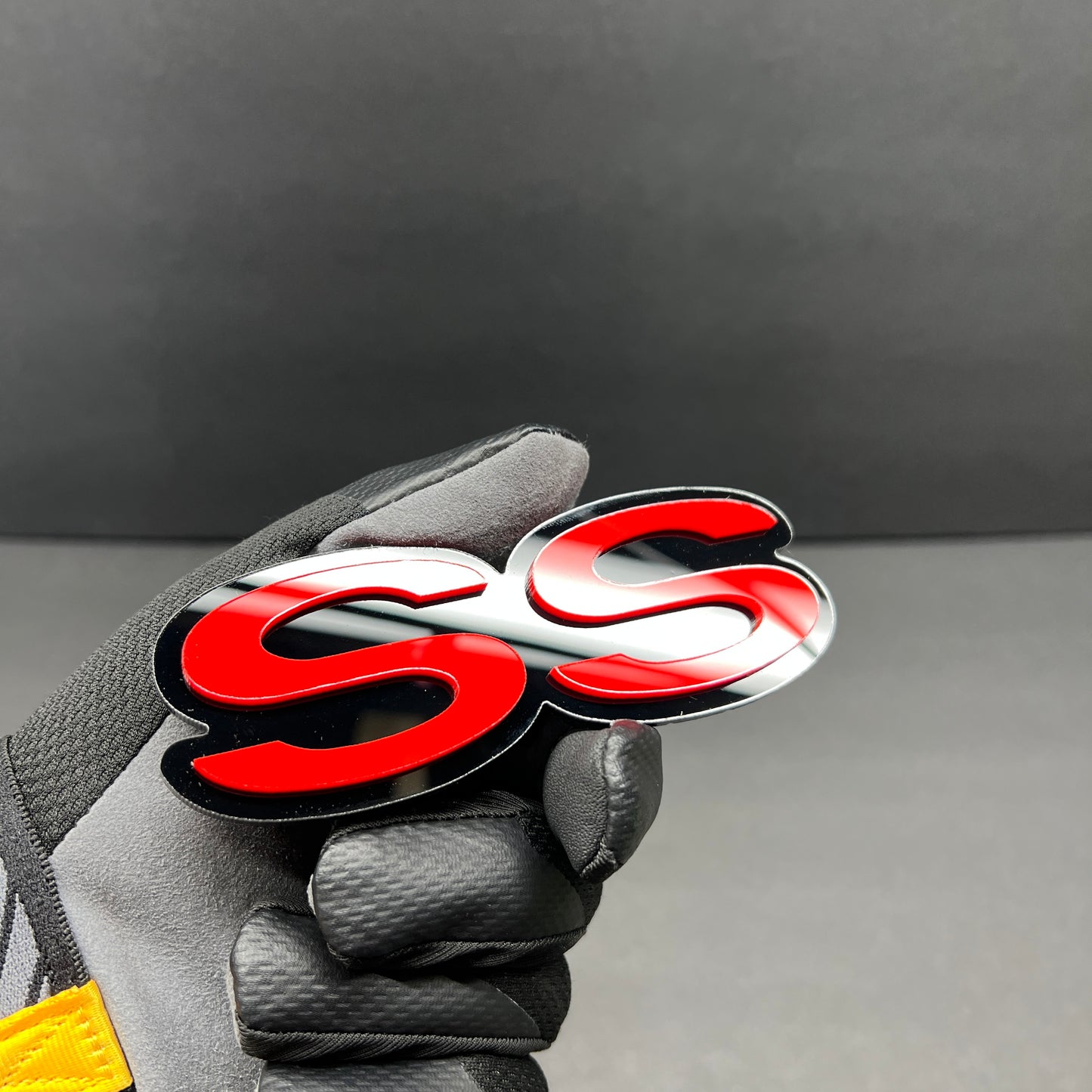 Close-up of SS text car badge in red with gloss black border.
